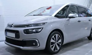 En ljusgrå mpv bil står i ett garage. Den har moderna strålkastare och snygga fälgar.