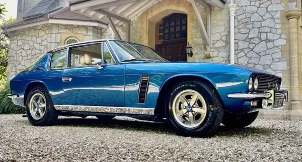Blå Jensen Interceptor parkerad framför ett stenhus.