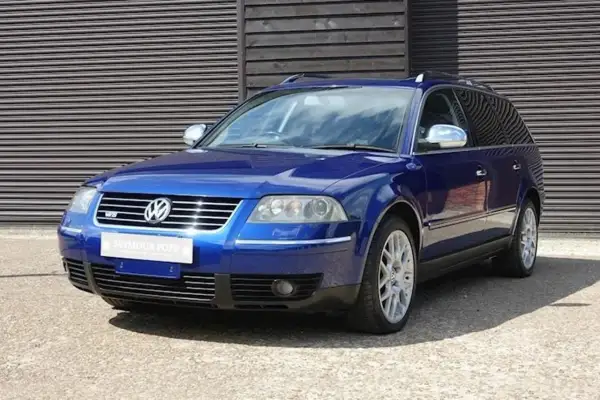 En blå Passat W8 kombi står parkerad framför en träfasad.