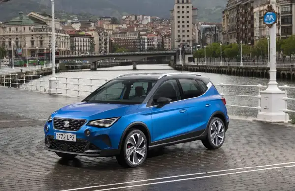 Blå Seat Arona parkerad vid en kaj med stad och broar i bakgrunden. Perfekt för en seat arona test i en europeisk stad.